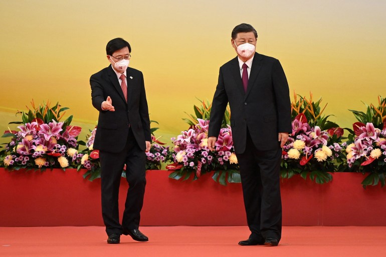 John Lee (on left) stands om a stage with Chinese president Xi Jinping