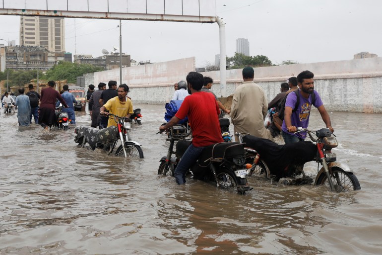 Karaçi'de muson mevsiminde sakinler su basmış bir yoldan geçiyor