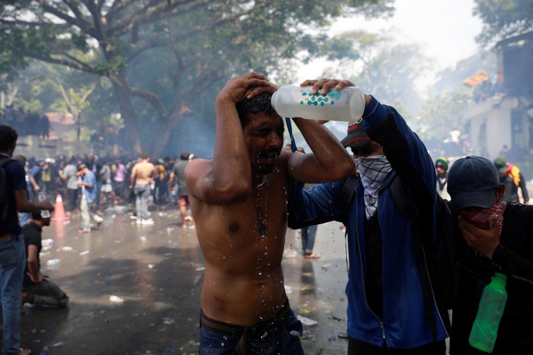 A demonstrator pours water on a man during a protest outside the office of Sri Lanka's Prime Minister