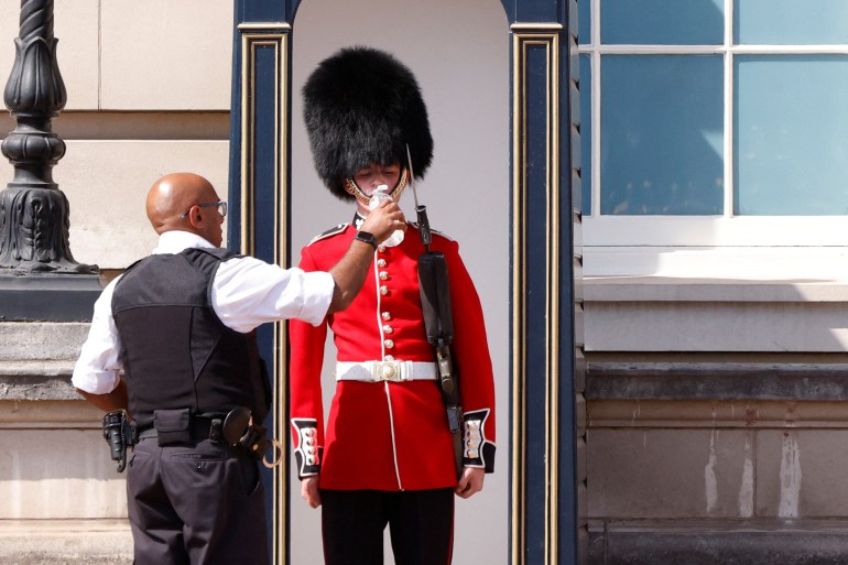 A member of the Queen's Guard receives water to drink during the hot weather, outside Buckingham Palace in London