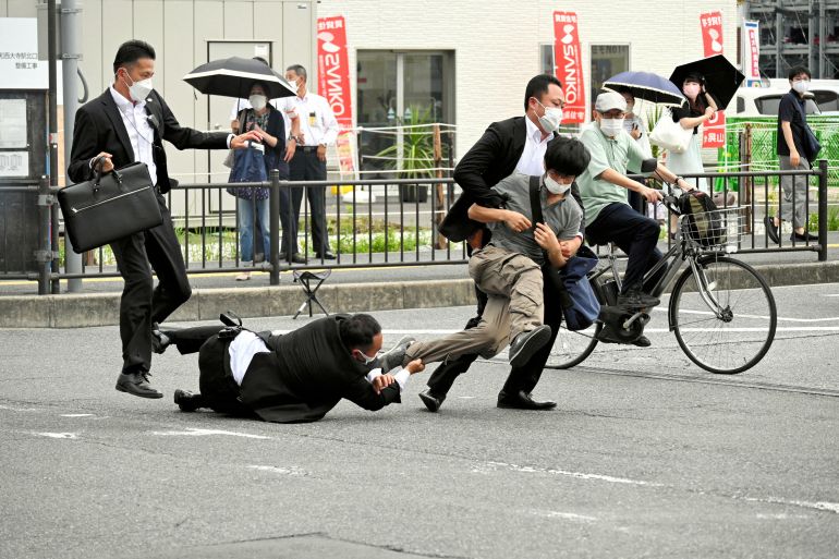 Security tackle a man in brown shirt and trousers on the street shortly after Shinzo Abe was shot