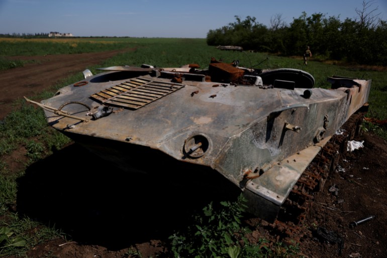 A Ukrainian soldier walks past destroyed Russian tanks in a field