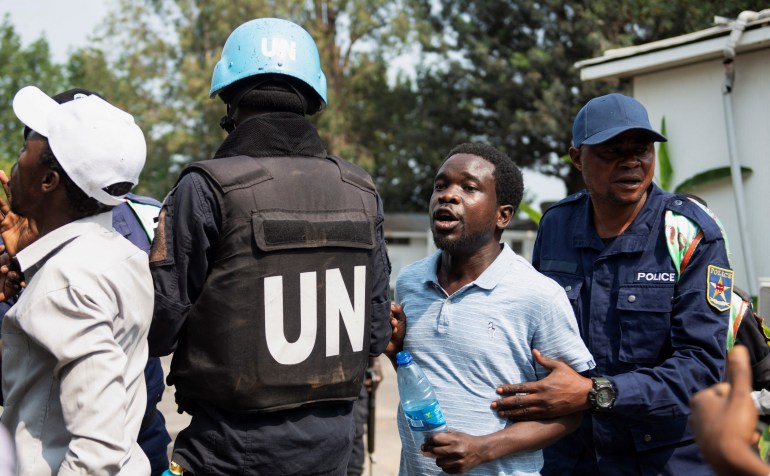 يحاول شرطي كونغولي وأحد أفراد حفظ السلام التابعين لبعثة الأمم المتحدة لتحقيق الاستقرار في جمهورية الكونغو الديمقراطية (MONUSCO) إيقاف المتظاهرين داخل مجمع مستودع لقوة حفظ السلام التابعة للأمم المتحدة في غوما في مقاطعة شمال كيفو بجمهورية الكونغو الديمقراطية