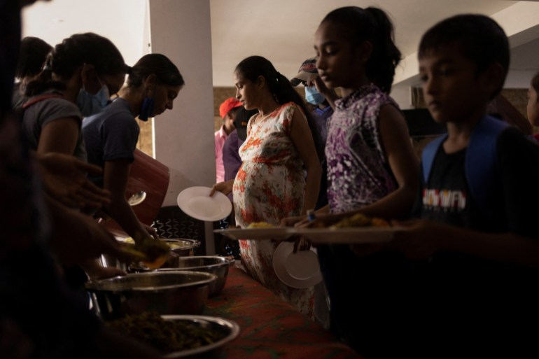 Oamenii stau la coadă în timp ce primesc mâncare la o bucătărie comunitară