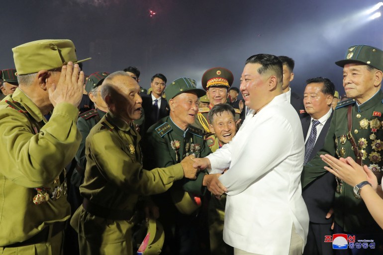 Kim Jong Un in a white shirt smiling as he shakes hands with a group of Korean War veterans - in uniform - during the Victory Day celebrations.