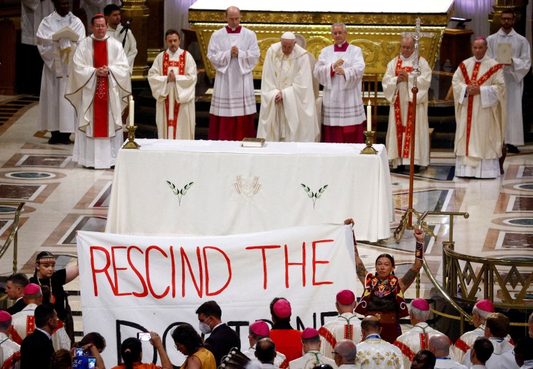 Indigenous people hold a banner reading 'Rescind the Doctrine' during a papal mass in Quebec