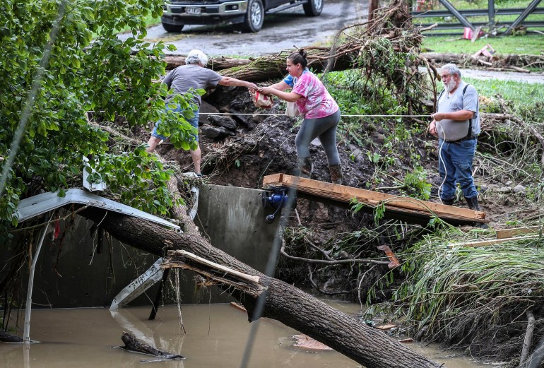 Perry County, Kentucky'deki şişmiş Grapevine Creek'in yanındaki düşmüş bir ağacın yanında üç kişi