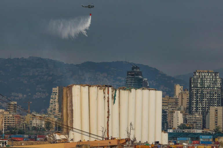 A helicopter drops water on Beirut's partially collapsed grain silos