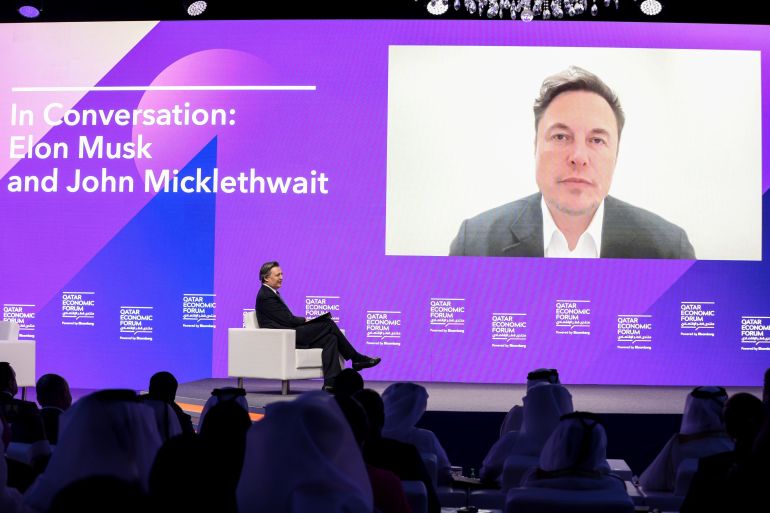 Elon Musk, chief executive officer of Tesla Inc., right, appears via video link alongside John Micklethwait, editor-in-chief of Bloomberg News, during the Qatar Economic Forum (QEF) in Doha, Qatar
