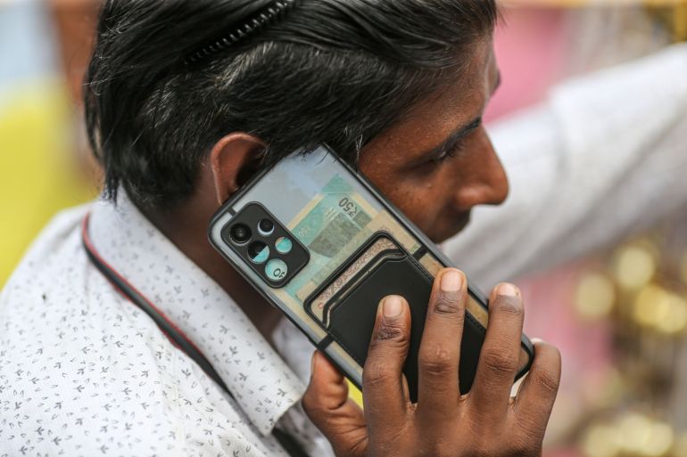 A person talks on a mobile phone with Indian rupee banknotes inside the phone case in Mumbai, India
