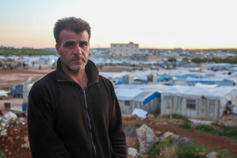 Photo montrant le déplacé syrien Ghassan Hammoud avec le camp de déplacés dans lequel il vit derrière lui