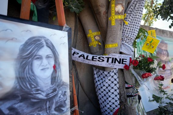 Yellow tape marks bullet holes on a tree and a portrait and flowers create a makeshift memorial at the site where Shireen Abu Akleh was shot and killed.