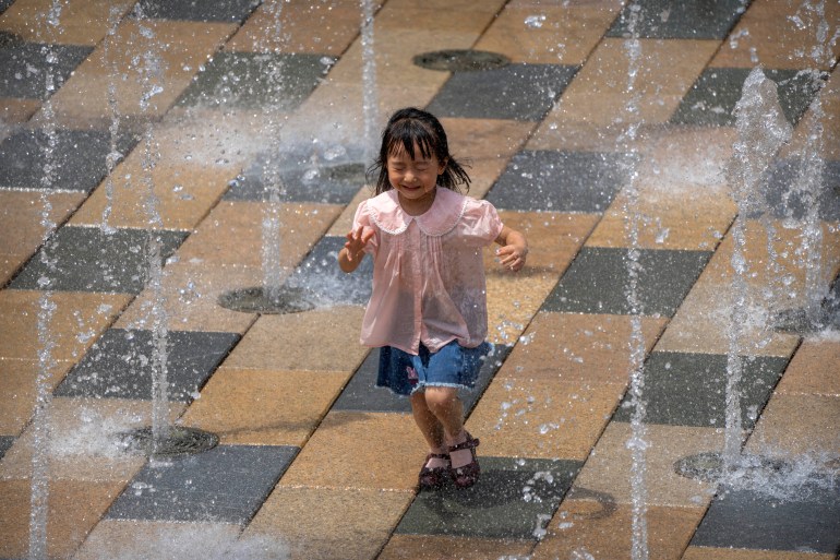 A girl runs through a fountain at an outdoor shopping area.