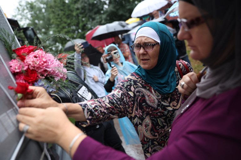 Women place flowers on a truck carrying 50 coffins with remains of the victims of the 1995 Srebrenica genocide in Visoko, Bosnia, Friday, July 8, 2022. The remains of the 50 recently identified victims of Srebrenica Genocide will be transported to the Memorial centre in Potocari where they will be buried on July 11, the anniversary of the Genocide [Armin Durgut/AP]