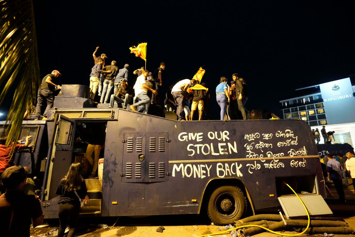 Protesters stand on a vandalised police water canon truck