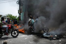 A motorcycle taxi driver carries clients past a burning barricade