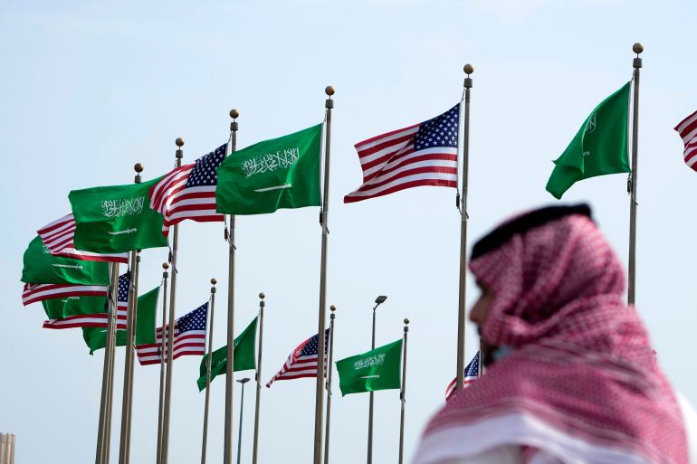 A man stands near Saudi and American flags