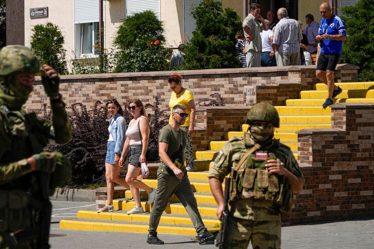 People walk past as Russian soldiers guard an office for Russian citizenship applications, in Melitopol, south Ukraine, Thursday, July 14, 2022. Russia took control of part of the Zaporizhzhia region quickly after the launch of the military operation in Ukraine. This photo was taken during a trip organized by the Russian Ministry of Defense. (AP Photo)