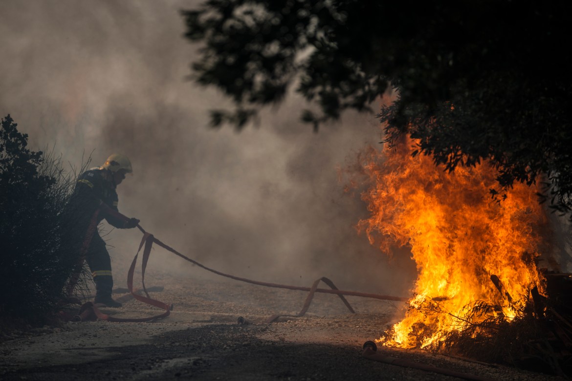 A firefighter pulls a hose as the fire burns near a house at Mount Penteli