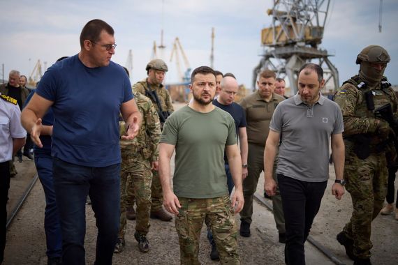 In this photo provided by the Ukrainian Presidential Press Office, Ukrainian President Volodymyr Zelenskyy, center, surrounded by ambassadors of different countries and UN officials, visits a port in Chornomork during loading of grain on a Turkish ship, background, close to Odesa, Ukraine