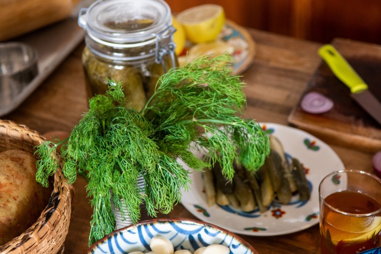 A view of some pickes and vase full of dill, with lemons and onions in the background