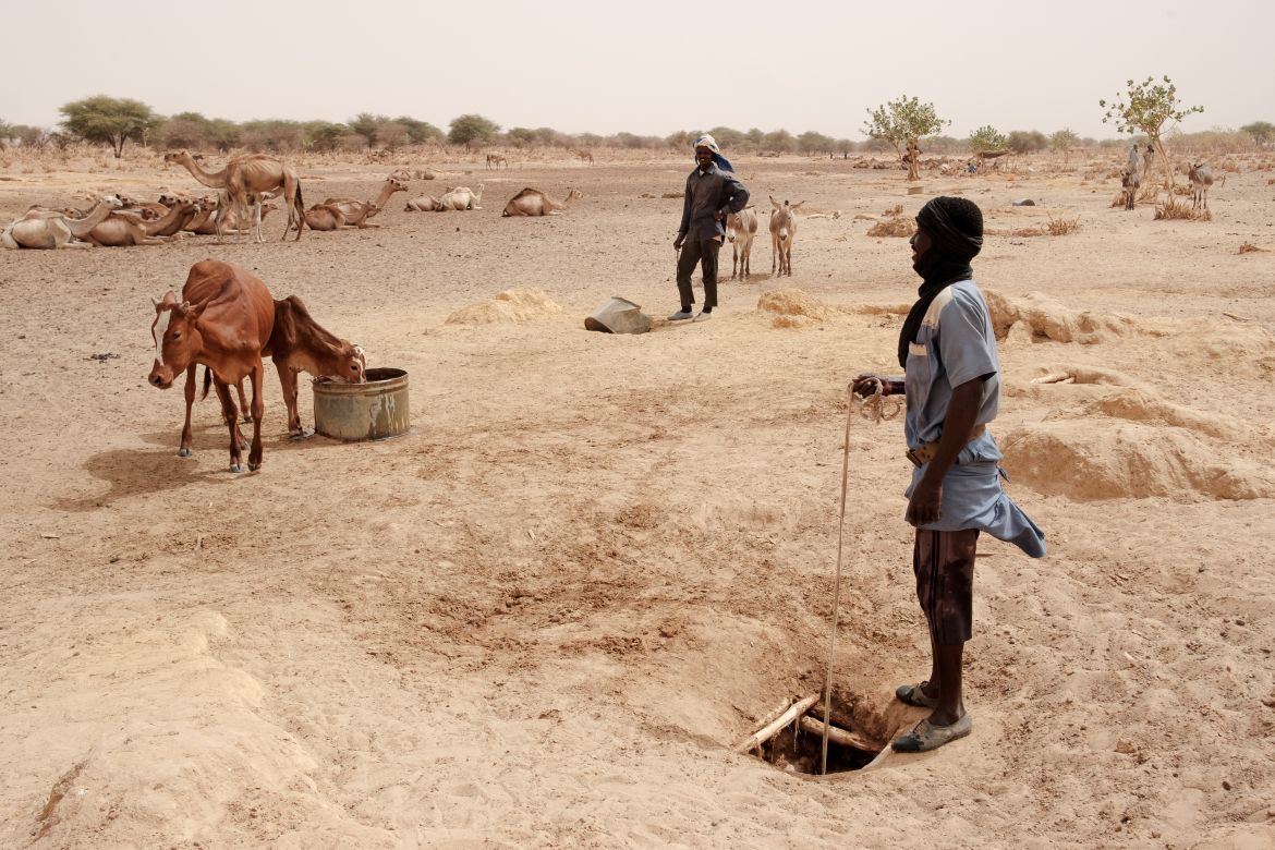 A herder stands pulling a bucket up from a hand dug well