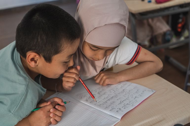 A photo of two children reading from one notebook.