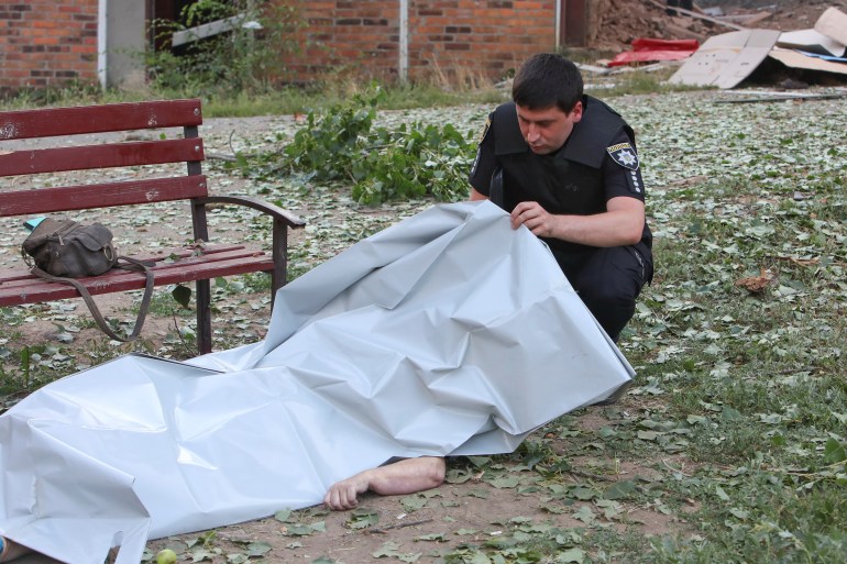 A police officer inspects the body of a woman killed during a Russian military raid in Kharkiv, Ukraine.
