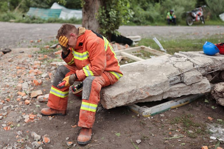A man sits as firefighters remove debris to find bodies of people at the Central House of Culture, after a military raid hit a building in Chuhuiv, Ukraine.