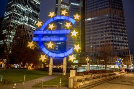 A man walks past the Euro sculpture in Frankfurt, Germany