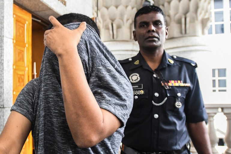 A man accused of sexual assault covers his face as he is escorted by a police officer at a court in Kuala Lumpur