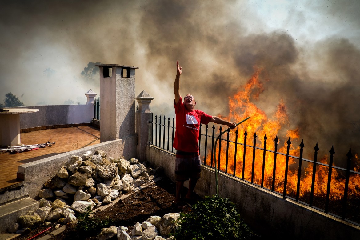 A inhabitant pours water onto the flames during a forest fire in Canecas, outskirts of Lisbon, Portugal