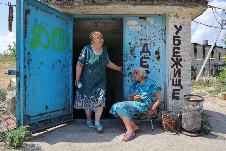 Two women in blue dresses outside a glass factory bomb shelter in the city of Lysychansk in the Luhansk Region, Ukraine.
