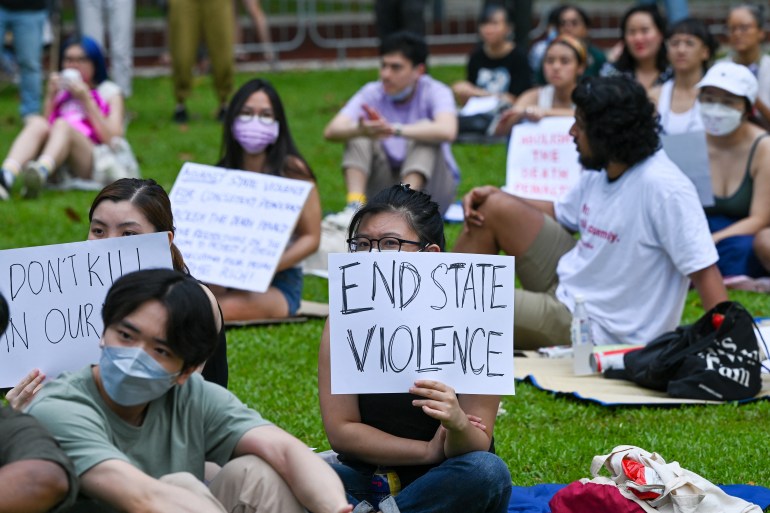 Singaporeans sit on the grass at 'Speaker's Corner', the only place protest is allowed in Singapore, to show their opposition to the death penalty. One sign being held up reads: "End State Violence".
