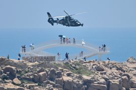 Tourists look on as a Chinese military helicopter flies past Pingtan island, one of mainland China&#39;s closest points to Taiwan [File: Hector Retamal/AFP]