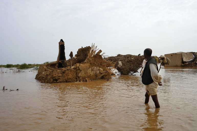 A Sudanese man walks through a flooded area on August 18, 2022 in the eastern state of Kassala, one of the badly affected regions in Sudan due to torrential rains this week. - The death toll from flooding has risen to more than 75 with heavy rain damaging tens of thousands of homes, according to police earlier this week, even though torrential rains usually fall in Sudan between May and October, when the country faces severe flooding, wrecking property, infrastructure and crops. (Photo by Hussein ERY / AFP)