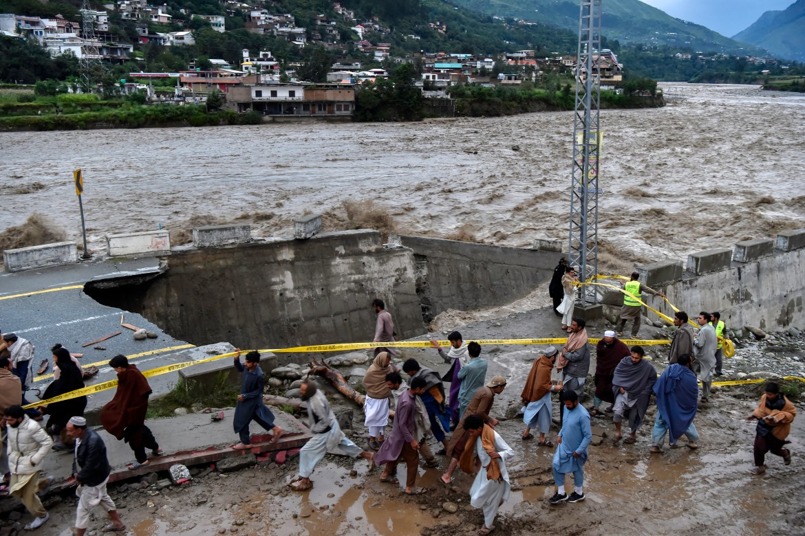 People gather in front of a road damaged by flood