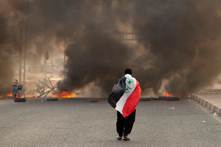 A supporter of Iraqi Shiite cleric Moqtada Sadr carries the Iraqi flag as he walks down a road blocked by burning tyres