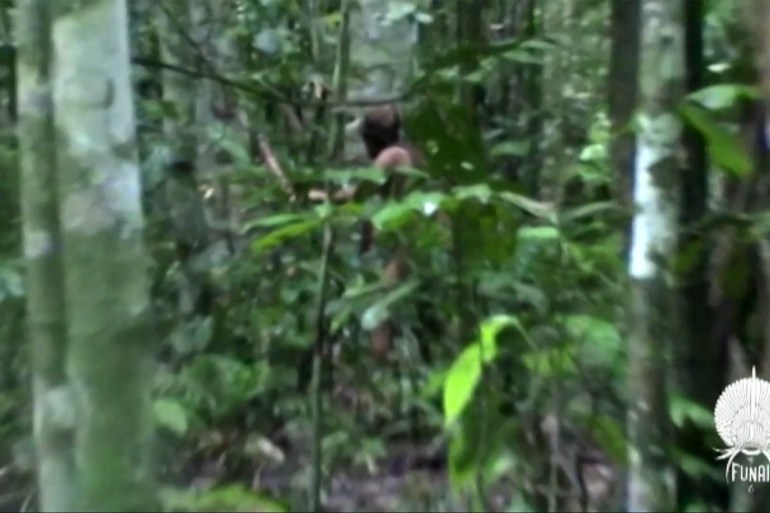 A glimpse of the Indigenous man through jungle trees and plants.