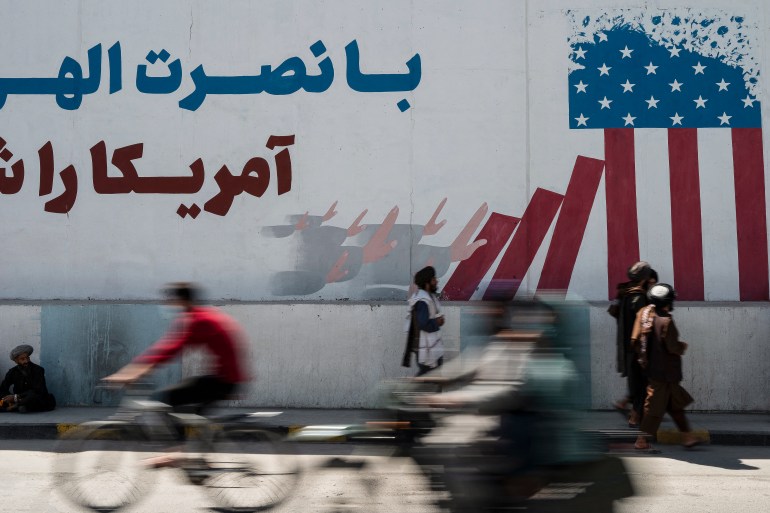 Taliban members walk past a mural depicting a US flag on the first anniversary of the withdrawal of US-led troops from Afghanistan, in Kabul on August 31, 2022. - The Taliban declared on August 31 a national holiday and lit up the capital with coloured lights to celebrate the first anniversary of the withdrawal of US-led troops from Afghanistan after a brutal 20-year war. (Photo by Wakil KOHSAR / AFP)