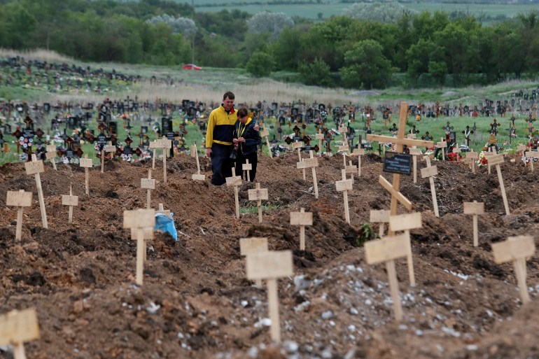 People stand amid newly-made graves at a cemetery in the course of Ukraine-Russia conflict in the settlement of Staryi Krym outside Mariupol,