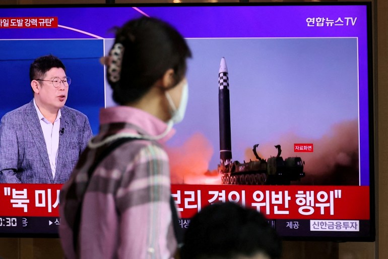 a man walks past a tv screen showing a north korean missile launch