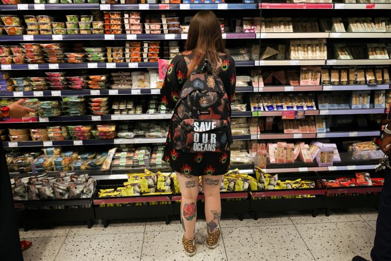 A person wearing a backpack with the slogan "SAVE OUR OCEANS", looks at food goods in a shop as UK inflation heads towards 10% in London, Britain,