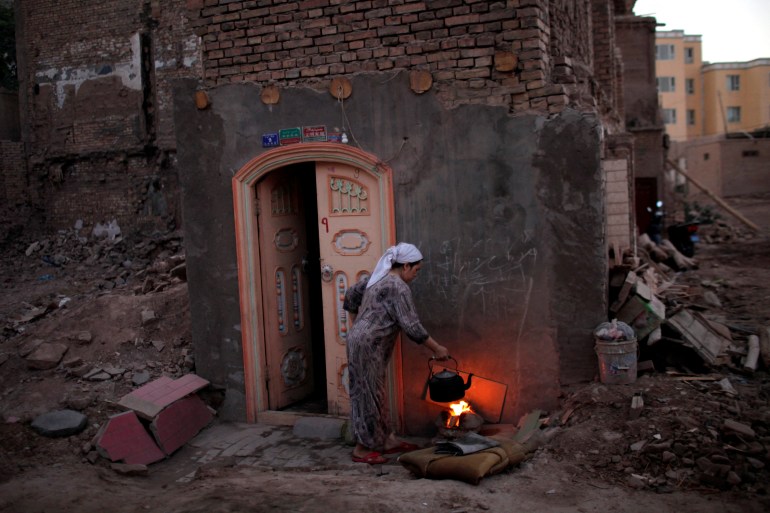 A woman cooks in her house next to the remnants of her demolished house in Xinjiang province.