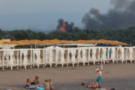 People rest on a beach as smoke and flames rise after explosions at a Russian military airbase, in Novofedorivka, Crimea on August 9 [Stringer/Reuters]