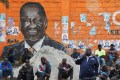 People sit next to a wall mural of Raila Odinga the presidential candidate for Azimio la Umoja and One Kenya Alliance in Kibera slums of Nairobi, Kenya.