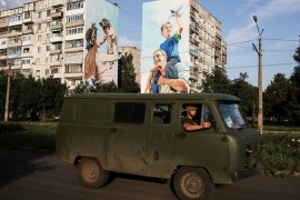 Ukraine servicemen drive past a mural of a family on damaged buildings in Bakhmut [File: Reuters]