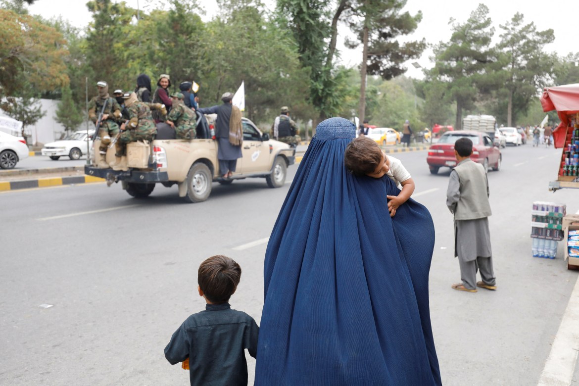 An Afghan woman walks with her children on the anniversary of the fall of Kabul