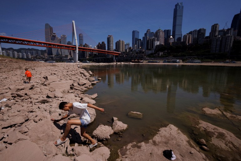 A boy climbs on the dried-up riverbed of the Jialing river, a tributary of the Yangtze, that is approaching record-low water levels in Chongqing, China [File: Thomas Peter/Reuters]