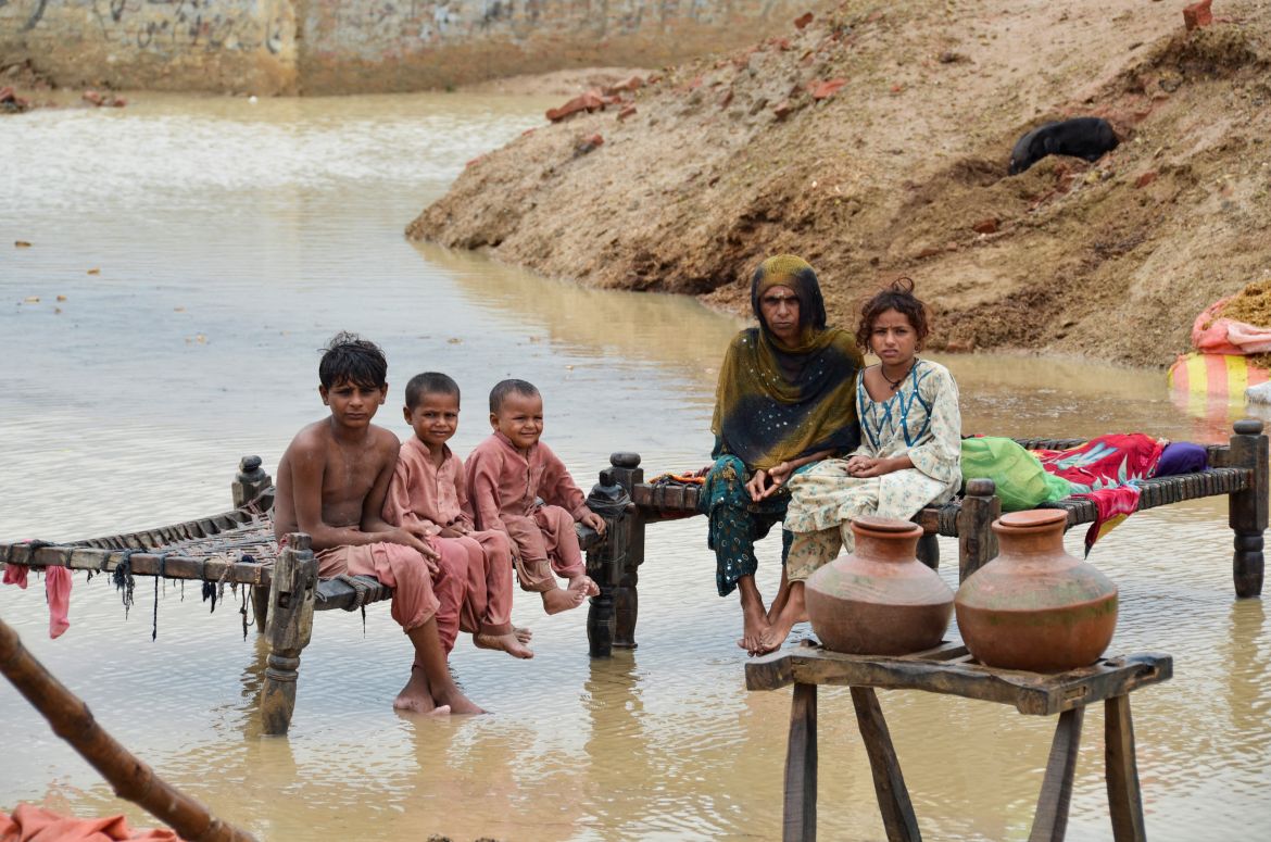 A woman and children sit on rope beds amidst rain waters besides their damaged house